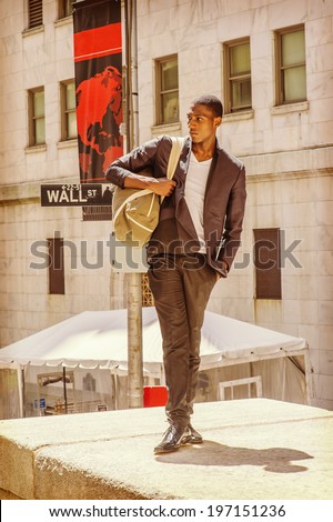 Street Fashion. Wearing a white under wear, fashionable jacket, pants, leather shoes, carrying a shoulder bag,  a young black college student is standing on Wall Street, confidently looking forward.