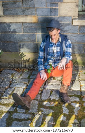 Man Missing you. Dressing in a pattern shirt, a hoodie vest,  jeans, leather boot shoes, wearing a woolen Fedora hat, a young guy is sitting on the ground, looking at a white rose,  thinking.