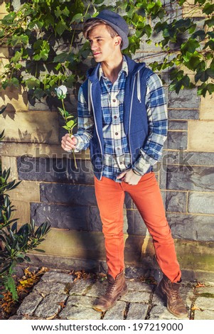 Man Casual Fashion. Dressing in blue, white pattern shirt, blue hoodie vest,  red jeans, brown leather boot shoes, wearing woolen Fedora hat, a young guy is holding a white rose, waiting for you.
