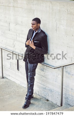 Young black man thinking outside. Wearing a white under wear, fashionable jacket, a young black college student is standing against the wall, seriously thinking. Street Fashion.