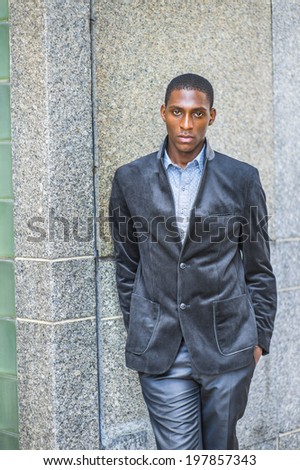 Young black man thinking outside. Dressing in a new style blazer, two hands putting in pockets, a young black guy is standing against the wall, seriously looking at you. Street Fashion.
