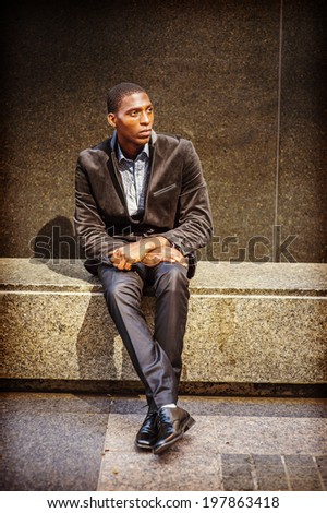 Young black man thinking outside. Dressing in a blazer, pants, leather shoes, a young black guy is sitting on a marble stone bench, looking up, waiting for you.