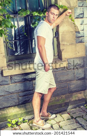Young man. Wearing a white V neck T shirt, light yellow shorts,  leather shoes, a young guy is standing by a window with green ivy leaves, looking down, thinking.