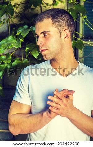 Portrait of young man, wearing a white V neck T shirt,  short hair, grasping hands.