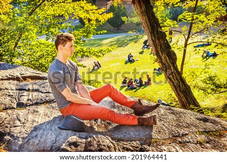 Man missing you. Dressing in a gray long sleeves with roll-tab Henley shirt, red jeans, brown boot shoes, a young guy is sitting on rocks, relaxing, thinking. some people sitting background grasses.