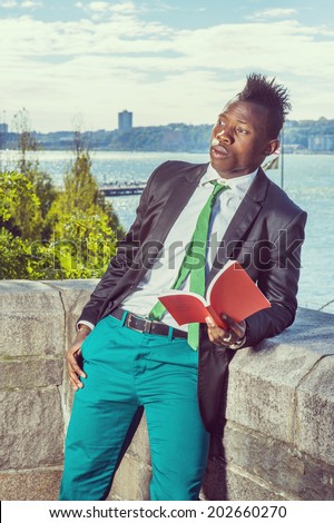 Man Reading Outside. Dressing in a white undershirt, a black blazer, green pants, a green tie, holding a red book,  a young black guy with mohawk haircut is standing by a river,  reading, thinking.