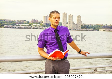 Young Man Reading Book Outside. Dressing in a purple shirt, a black neck tie, a hand holding banister, frowned, a young sexy guy with beard, mustache is reading a red book by the river, thinking.