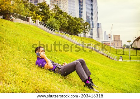 Man Taking a Break.  Dressing in a purple shirt, gray pants, a black tie, leather shoes, a young handsome businessman is lying on grasses, talking on a mobile phone.