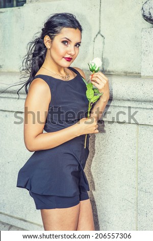 Flower Girl. Dressing in black, sleeveless top, short pants, necklace, a young pretty lady is standing by an old fashion wall, holding a white rose, waiting for you.
