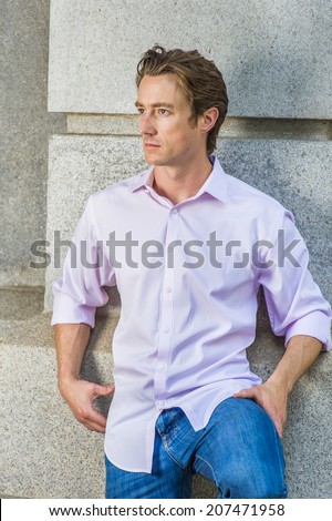 Man Thinking Outside. Wearing a light pink, long sleeve shirt, blue jeans, bending a leg, a young handsome guy is standing against a concrete wall, looking around, thinking