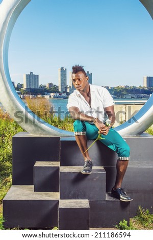 Man Thinking of You. Dressing in white shirt, green pants, leather shoes, holding a white rose, a young black guy with mohawk hair is sitting by ring structure, waiting for you. Urban Casual Fashion.