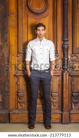 Portrait of Young Businessman. Wearing a white shirt, black pants, leather shoes, a young college student is standing by an old fashion style office door, hands in pockets, thinking.