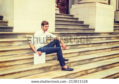 College Student Relaxing Outside. Wearing a white shirt, black pants, leather shoes, holding a white book, a young handsome guy is sitting on stairs outside an office building, relaxing, thinking.