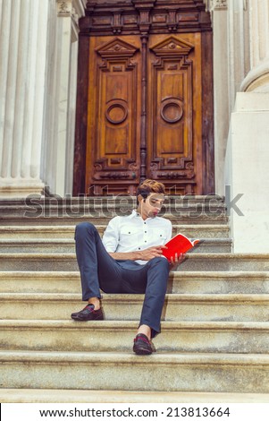 College Student. Wearing a white shirt, black pants, leather shoes, holding a red book, a young handsome guy is sitting back on stairs outside an office building, relaxing, reading, thinking.