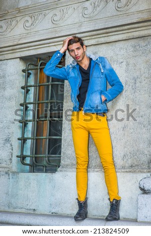 Man Casual Fashion. Dressing in a blue jacket with hood, black underwear, yellow pants, leather boot shoes, a young handsome guy is standing by a window, a hand scratching head, waiting for you.