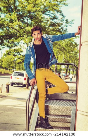 Worker Relaxing on Street. Dressing a blue jacket with hood, black under wear, yellow pants, leather boot shoes, a young handsome guy is standing by railing in the front of office door way, relaxing.
