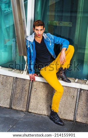 Man Thinking about You. Dressing a blue jacket with hood, black under wear, yellow pants, leather boot shoes, a young handsome guy is sitting by metal structure, against a glass wall, waiting for you.