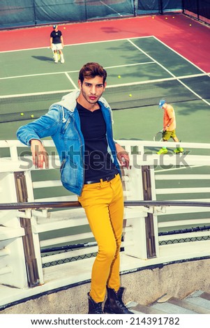 Man Waiting for You. Dressing in a blue jacket with hood, yellow pants, leather boot shoes, a young handsome guy is standing by a tennis court, stretching arms on railing, passionately looking at you.