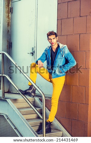 Portrait of Young Worker. Wearing a blue jacket with hood, black underwear, yellow pants, leather boot shoes, a young handsome guy is standing by railing in the front of office door way.