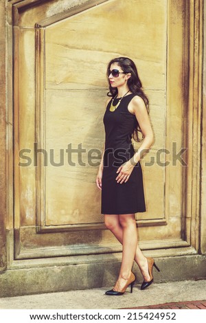 Business Lady. Dressing in black work dress, wearing sunglasses, a necklace with golden pendant, leather shoes, a young sexy businesswoman is standing outside, taking a break. Instagram effect.