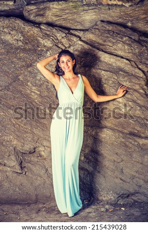 Portrait of Pretty Lady. Dressing in a light blue, v neck, long dress, a young sexy woman is standing by rocks, smiling, charmingly looking at you.