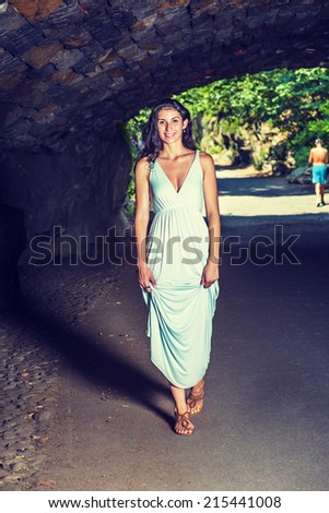 Pretty Lady Walking in Dark. Dressing in a light blue, v neck, long dress, wearing brown sandals, a young sexy woman is waking through a tunnel.
