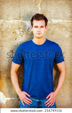 Portrait of Young Sexy Man.  Wearing a blue T shirt, jeans, a young handsome guy is standing against a old concrete wall, confidently looking at you.