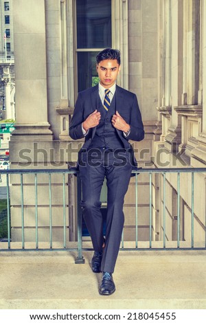 Young Business Man. Dressing in a black suit, patterned necktie, vest, leather shoes, a young college graduate student is sitting by railing in an old style office building, relaxing, thinking.