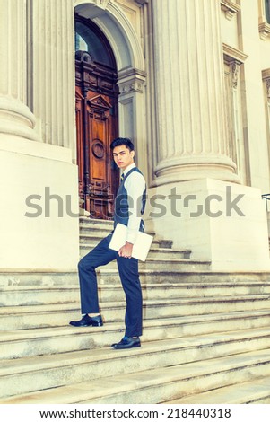 College Student. Dressing in white shirt, black vest, pants, leather shoes, patterned necktie, holding a laptop computer, a young businessman is walking up stairs outside an office, looking at you.
