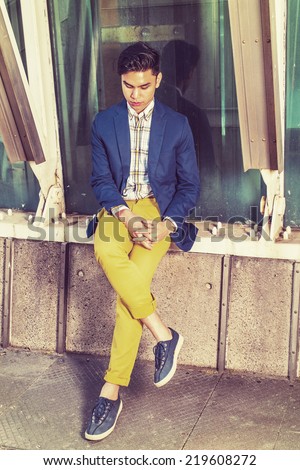Lonely Man. Dressing in blue blazer, patterned under wear, yellow pants, sneakers, crossing hands, legs, lowering head,  a young guy is sitting by metal structure, against glass wall, sad, thinking.