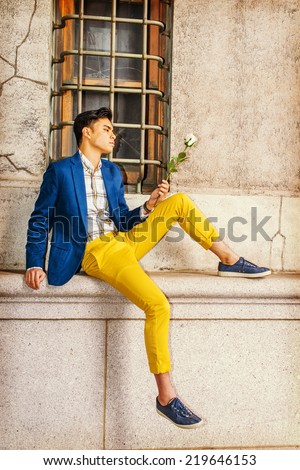 Man Missing You. Dressing in blue blazer, yellow pants, casual sneakers, a young handsome guy is sitting by a window on street, looking down at white rose on hand, thinking. Man Casual Fashion