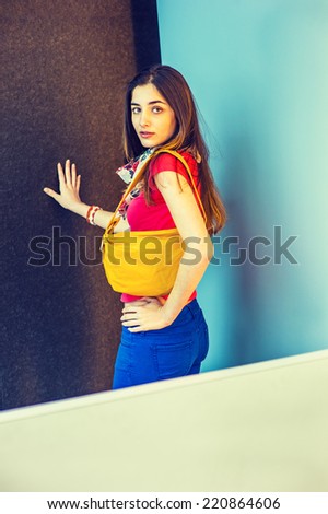 Professional Woman. Wearing red short sleeve shirt, light weight scarf, blue pants, shoulder carrying a yellow leather small bag, a beautiful lady standing in modern interior, looking at you.