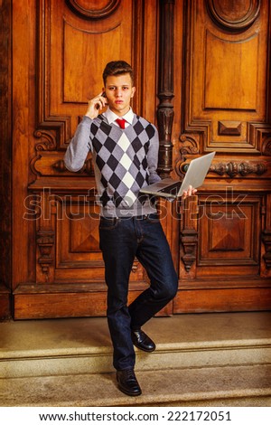 Busy Student. Wearing a patterned sweater, red tie, blue jeans, leather shoes, a young guy is waling down from office, talking on his mobile phone, working on a laptop computer in the same time.