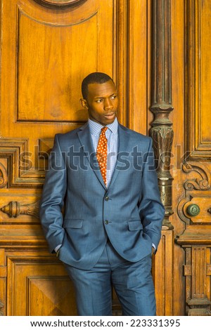 Portrait of Businessman. Dressing formally in blue suit, patterned shirt and necktie, short haircut, hands in pockets, a young guy is standing in the front of an old style office door, thinking.