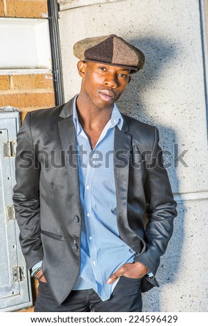Portrait of Young Black Guy.  Wearing fashionable Newsboy cap, black blazer, unbuttoned, a young black guy is standing on the corner of the street, looking at you. Man Urban Fashion.