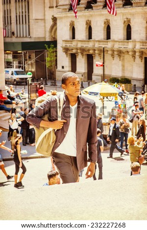 Man Traveling. Carrying a shoulder bag, walking up on steps, a young black college student is traveling on street in a big city. Many people on background.