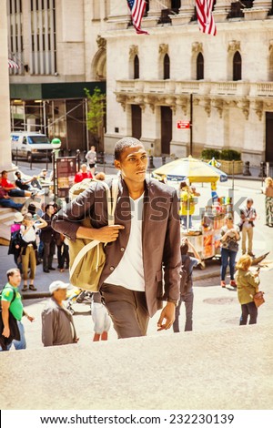 Man Traveling. Carrying a shoulder bag, walking up on steps, a young black college student is traveling on street in a big city. Many people on background.