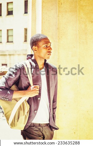 Man Traveling. Carrying a shoulder bag, a young black college student is walking though columns on campus, sad, thinking, lost in thought.
