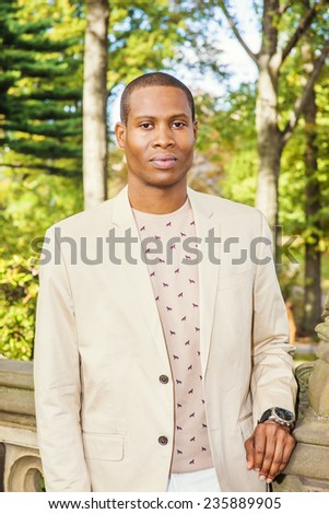Portrait of Young Black Business Man. Dressing in cream blazer, collarless sweater, wearing wristwatch, A young black graduate student is standing on campus, seriously looking at you.