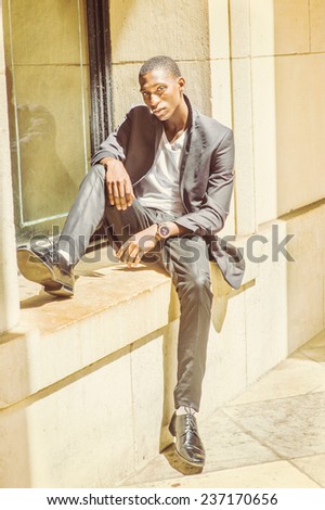 Street Fashion. Dressing in white under wear, fashionable jacket, pants, leather shoes, wearing wristwatch, a young black college student is sitting against a window frame, relaxing, waiting for you.