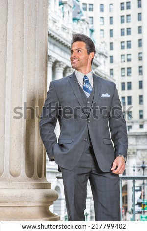 Way to Success. Dressing in dark blue three piece suit, necktie, wearing wristwatch, a handsome, sexy, middle age businessman is standing in the front of office building, confidently looking up.