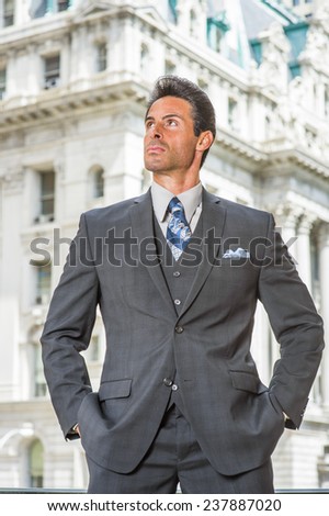 Man Power. Dressing in dark blue three piece suit, necktie, hands in pockets, a handsome, sexy, middle age businessman is standing outside office building, confidently looking up.