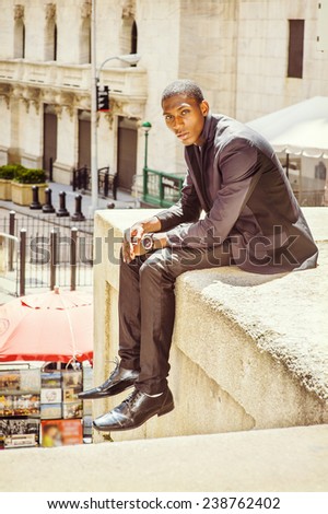 Young man thinking on street. A young black college student is sitting outside, arched the back, holding hands on the laptop, under strong sunshine, relaxing.