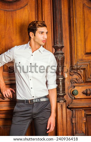 The Door to Success. Wearing a white shirt, black pants, a young college student is standing by an old fashion style office door, confidently looking forward. Portrait of Young Business Man