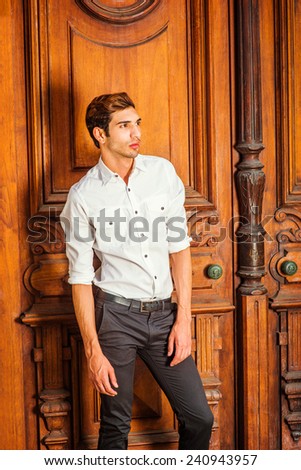 The Door to Success. Wearing a white shirt, black pants, a young college student is standing by an old fashion style office door, confidently looking forward, thinking. Man Casual Fashion