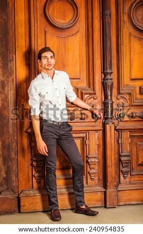 The Door to Success. Wearing a white shirt, black pants, leather shoes, a young college student is standing by an old fashion style office door, a hand resting on door knob, looking up, thinking.