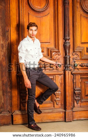 Man Casual Fashion. Wearing a white shirt, black pants, leather shoes, a young college student is standing by an old fashion style office door, a hand holding door knob, bending leg, waiting for you.