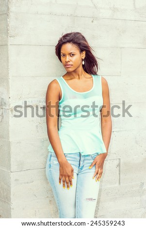 Girl Waiting for you. Wearing a green tank top, drop earrings, blue jeans, a young pretty woman is standing against the wall outside in the wind, waiting for you. Modern woman casual fashion