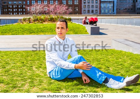 Wearing white shirt, blue pants, white sneakers, a young guy sitting on lawn under sunshine in spring, thinking. A woman with children strollers on background. Concept of missing family, friendship.