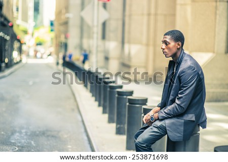 Man thinking outside. Young black teenage boy is sitting on street, hunchbacked, sad, tired, looking down, thinking, lost in thought. Retro filtered look.